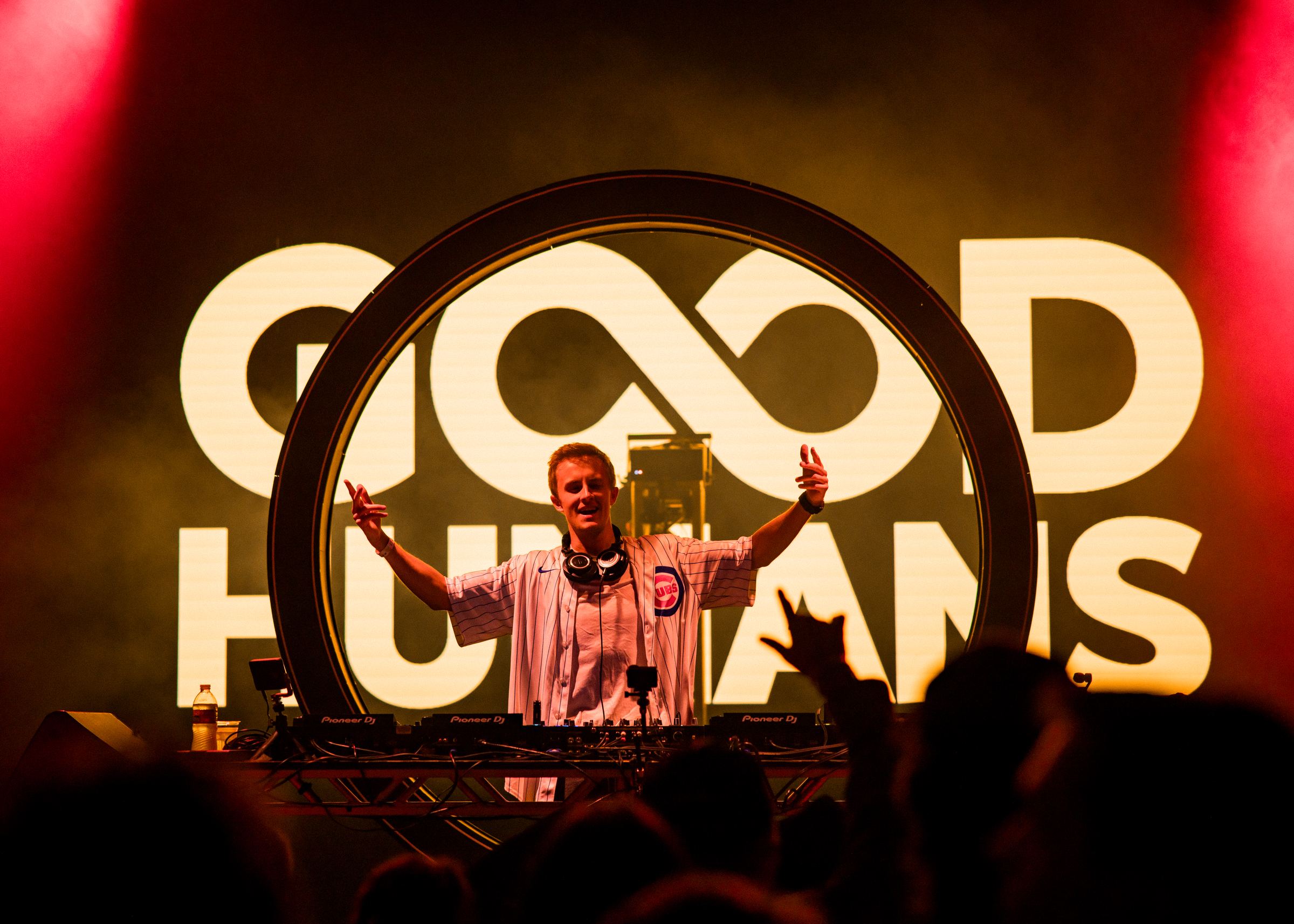 Alex on stage in a Cubs jersey in front of the Good Humans logo, crowd in the foreground