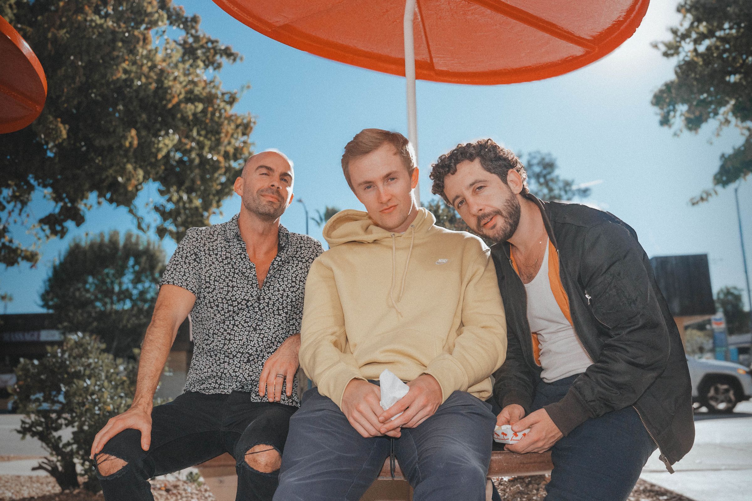 Peter, Alex and Mickey on a bench under an orange umbrella outside In-N-Out